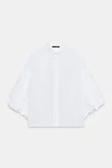 Camisa de algodón con cuello solapa y cierre frontal con botones ocultos. Presenta mangas abullonadas por debajo del codo con terminación elástica.