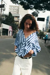 Camisa de rayas verticales azules y celestes, con cuello solapa, escote en V, cierre frontal con botones y mangas largas abullonadas con puños ajustados.