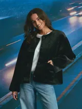 Campera de textura afelpada en color negro, con cuello redondo, cierre frontal con botones y bolsillos delanteros. Presenta detalles de terminaciones en material sintético liso a lo largo de la abertura y los bolsillos.