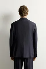 Blazer de corte relaxed fit confeccionado en tejido con lana, con solapas de muesca, manga larga con botones en los puños, bolsillos con solapa en la cadera, un bolsillo de vivo en el pecho y cierre frontal con dos botones.