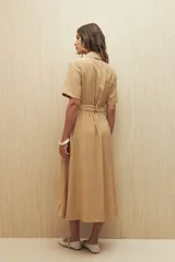 Vestido camisero midi color beige, con cuello clásico, mangas cortas y cierre frontal de botones. Incluye un cinturón ajustable de la misma tela con hebilla decorativa para marcar la cintura.