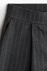 Pantalón de vestir gris oscuro, corte ancho y tiro alto, con pinzas frontales y finas rayas verticales blancas (pinstripe).