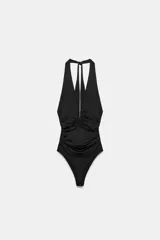 Body de cuello halter con espalda descubierta, confeccionado en mezcla de poliamida. Presenta un diseño drapeado en los laterales y una abertura frontal con aplicación metálica forrada. Cuenta con cierre de botones a presión en el bajo y lazada en el cuello.