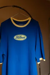 Remera oversize de algodón elastizado, color azul vibrante, con cuello redondo ribeteado en color beige claro. Presenta un estampado frontal ovalado en color beige claro con la palabra "Hermod" en tipografía cursiva.