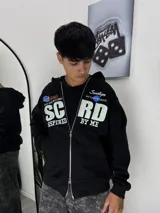 Campera con capucha negra de corte holgado, con cierre frontal doble y estampado gráfico en el pecho con letras blancas y detalles en azul.