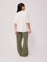 Remera color amarillo pastel con estampado de palmeras, flores de hibisco y texto 'California Ride the Tide Rusty Tribe'.