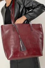 Bolso tipo tote grande confeccionado en cuero vacuno con textura efecto reptil. Presenta detalles de costuras artesanales en los laterales, doble asa de hombro y un colgante decorativo de borla de flecos de cuero.