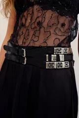 Cinturón ancho de cuero de búfalo negro con textura efecto cocodrilo, diseño multipuntada con hebillas dobles delanteras y apliques metálicos plateados en el lateral.