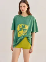 Remera oversize de corte cuadrado, color verde, con cuello redondo y estampa retro centrada en tono amarillo.