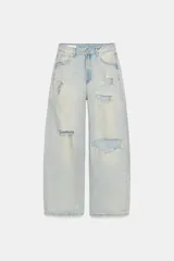 Jeans de tiro medio con corte baggy y diseño de cinco bolsillos. Presenta roturas localizadas en las piernas y cierre frontal con cremallera y botón metálico.