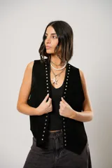 Chaleco de cuero descarne color tostado, con diseño oversize y terminación en picos. Presenta tachas metálicas a lo largo de la abertura frontal y flecos en la espalda.