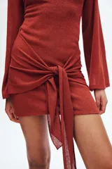 Vestido corto de punto texturizado en color terracota, con escote bote, mangas largas amplias y detalle de tiras anchas para anudar en la cadera.