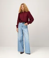 Camisa de crepé color blanco, con cuello inglés, manga larga abullonada con puños abotonados y cierre frontal oculto con botón diferenciado en el cuello.
