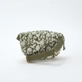 Riñonera de diseño acolchado en color verde kaki con estampado floral blanco. Cuenta con cierre superior metálico dorado y correa ajustable de cinta tejida al tono.