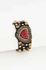 Pulsera de cuero sintético negro con un diseño central de corazón bordado en strass rojos y plateados. La banda está adornada con piedras de cristal en tonos ámbar y transparentes, junto con tachas metálicas en forma de estrella. Posee un cierre ajustable con botones a presión.