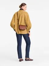 Cartera crossbody pequeña de cuero color marrón, de diseño estructurado con solapa frontal, botón a presión dorado y correa fina ajustable.