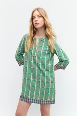 Túnica verde con estampa geométrica de cuadrados en verde más oscuro y blanco. Tiene escote en V con ribete marrón y mangas tres cuartos con ribete geométrico en puños y ruedo.