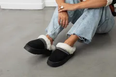 Pantuflas tipo slipper de gamuza negra con plataforma, forradas en su interior con piel sintética blanca y detalle de costura decorativa en el borde.