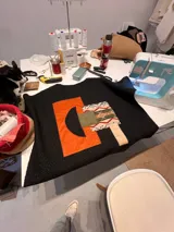 Campera de paño negro con diseño de collage frontal compuesto por formas geométricas en colores naranja, verde oliva y una pieza con estampado étnico. Presenta un diseño artesanal y único.