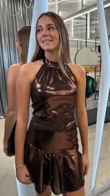 Vestido corto de fiesta color chocolate con acabado metalizado brillante. Presenta un diseño con cuello halter, ajuste al cuerpo y un detalle de volado en el ruedo.
