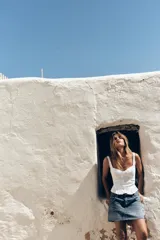 Top blanco estilo corsé con escote corazón, tirantes finos y bordados a tono. Presenta un bajo con volantes y cierre frontal con ganchos metálicos. La espalda es de tejido elástico tipo nido de abeja.