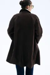 Abrigo largo hasta la rodilla, color marrón oscuro, con acabado cepillado suave. Presenta cuello camisero, manga raglán, botonadura frontal y bolsillos laterales insertados. Tiene forro interior y abertura en la espalda.