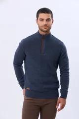 Buzo de punto color beige, con cuello alto y cierre frontal con cremallera y solapa de gamuza con botón. Presenta un tejido texturizado en el cuerpo y mangas lisas.