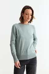 Sweater de punto fino color verde menta o celeste pálido, con cuello redondo y manga larga. Los puños tienen aberturas decoradas con pequeños botones dorados.