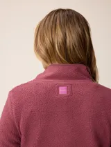 Canguro de sherpa color bordó, con cuello alto y cierre frontal parcial. Presenta un bolsillo con cierre en el pecho y bolsillos laterales, confeccionado en tejido de textura suave y abrigada.