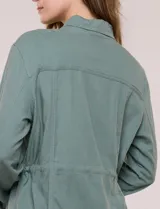 Sobrecamisa beige de lino liviano, con cuello camisero, cierre frontal de botones carey y bolsillos en el pecho. Cuenta con cordón ajustable en la cintura y mangas largas.