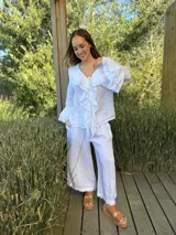 Camisa de lino azul marino con volados en cascada a lo largo del frente y en los puños de las mangas largas. Presenta un escote en V con un botón de nácar visible.