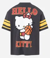 Remera gris oscuro de algodón con corte boxy, cuello redondo y mangas cortas con rayas amarillas. Estampado trasero de Hello Kitty jugando al baloncesto con letras rojas.