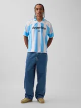 Camiseta de fútbol estilo retro de la selección argentina, con diseño de rayas verticales blancas y celestes. Presenta cuello polo, mangas cortas y el texto 'Argentina' estampado en el pecho junto a una pequeña bandera nacional. Incluye etiqueta oficial de FIFA Classics en el ruedo.