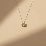 Collar con dije circular de diseño minimalista, elaborado en una combinación de plata y oro, con una circonia central engastada.