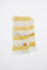 Bufanda larga de mohair y lana a rayas horizontales color crudo y amarillo, con flecos en los extremos y etiqueta de cuero con logo de la marca Bimba y Lola.