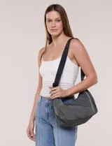 Cartera bandolera confeccionada en lona, de silueta en forma de medialuna y color gris. Presenta cierre superior negro y correa ajustable combinada para llevar cruzada o al hombro.
