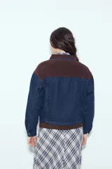 Campera de jean color negro con cuello de pana en tono marrón, cierre frontal con botones y bolsillos en el pecho. Presenta un diseño de corte relajado y ligeramente cropped, con interior forrado en corderito para mayor abrigo.