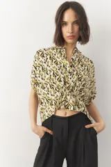 Blusa corta de manga corta con estampado en blanco y negro, cuello mao y cierre frontal con botones. Cuenta con detalle de elástico fruncido en la cintura que genera un efecto peplum.