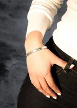 Pulsera esclava abierta de acero quirúrgico plateado con diseño labrado.