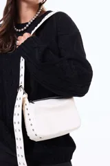 Bandolera de color blanco con cierre superior y correa ancha ajustable con ojales metálicos decorativos.