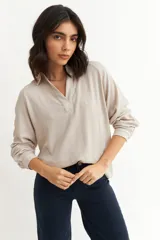 Blusa de textura arrugada en color beige, con cuello polo y mangas ranglán largas con puños elásticos.