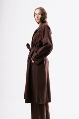 Trench de algodón color marrón chocolate, con solapas amplias, cierre cruzado con botones y cinturón ajustable a la cintura. Presenta mangas largas con trabillas en los puños y un corte holgado de largo midi.