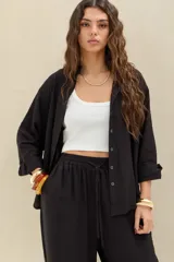 Camisa negra de manga larga, corte oversize, con cierre frontal de botones y cuello camisero.
