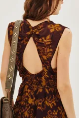 Vestido largo sin mangas con escote en V profundo y lazo ajustable en la cintura. Presenta un estampado geométrico en tonos marrón y ocre sobre fondo oscuro, con falda amplia y fluida.