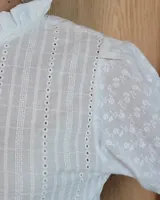 Camisa de manga larga con estampado de rayas verticales en tonos crudo y beige. Presenta cuello alto con volados, cierre frontal con botones dobles y puños con volados.