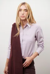 Camisa blanca de manga larga con cuello clásico y botones frontales. Tiene un bolsillo en el pecho con un pequeño logo bordado.
