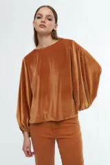 Blusa de terciopelo color ocre, con mangas largas abullonadas y puños elásticos. Presenta un corte holgado y cuello redondo.