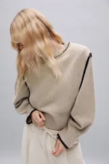 Jersey de punto color beige con cuello redondo y mangas largas abullonadas. Presenta detalles de vivos en color negro en el cuello, hombros y puños.