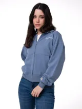 Buzo con cierre frontal completo, confeccionado en tejido French Terry color azul grisáceo. Presenta cuello alto, mangas largas con puños elásticos y logo de la marca bordado en el pecho y en el puño.