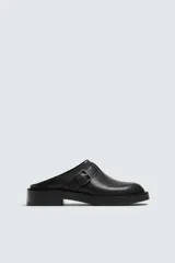 Zueco destalonado negro con hebilla en el empeine y suela a tono con tacón bajo.